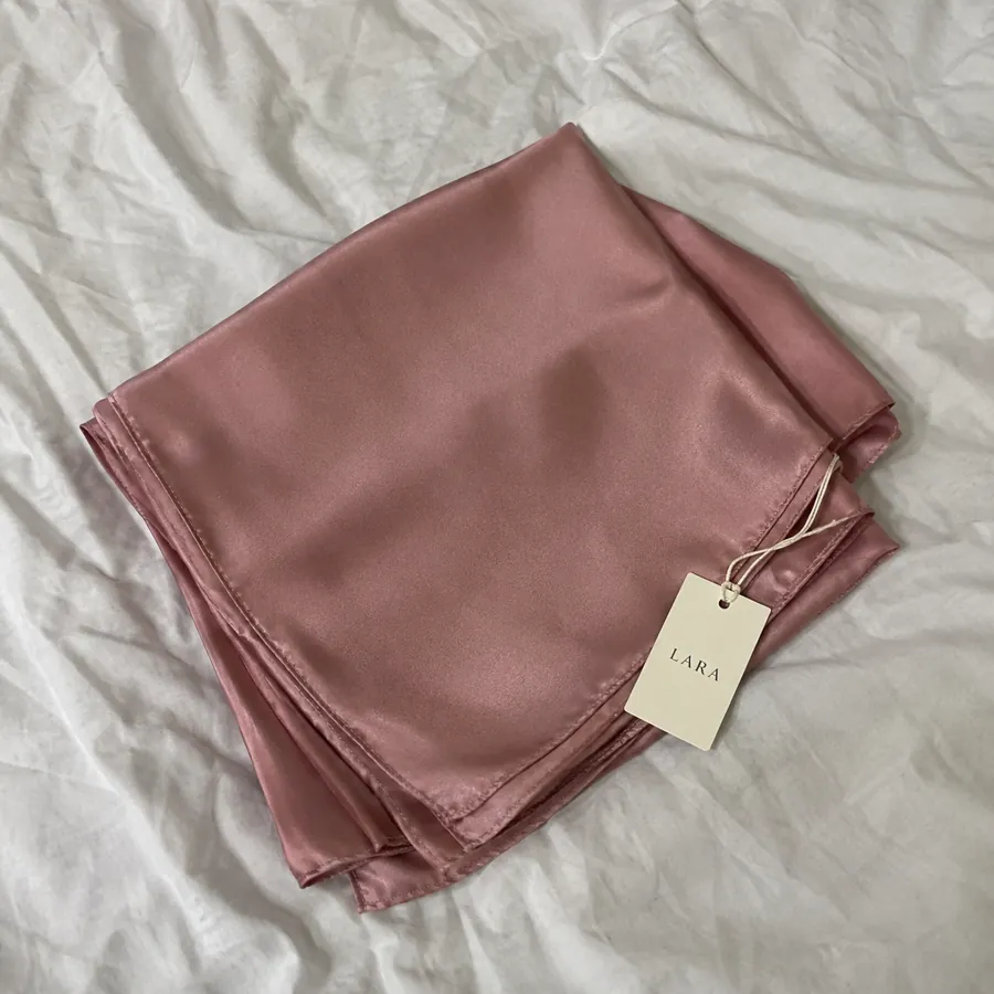 Demo stand-in for a seller's phone photo: LARA tudung folded on a bed
